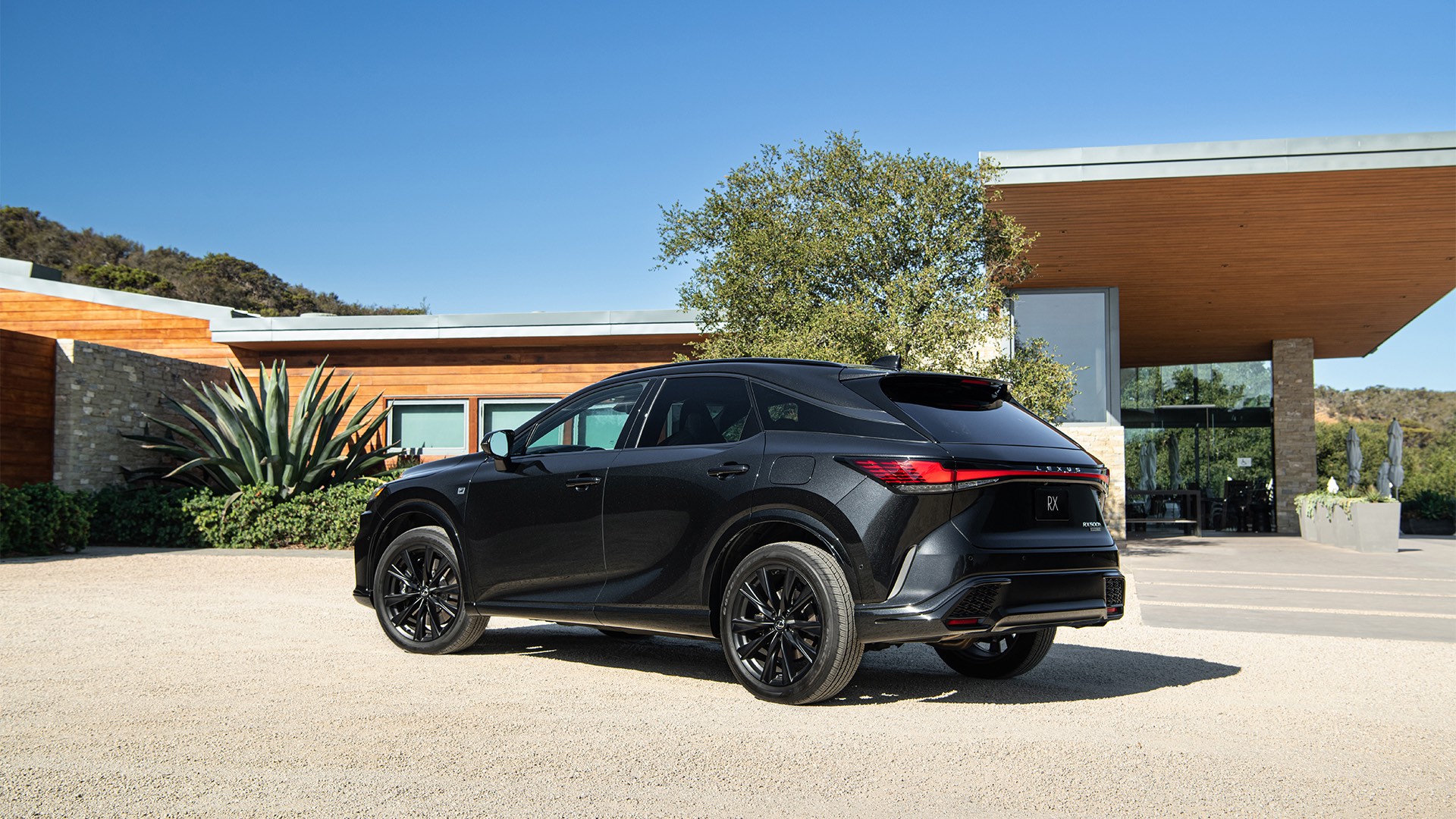 A Lexus RX 500h F Sport Performance in Graphite Black is parked on a gravel driveway 