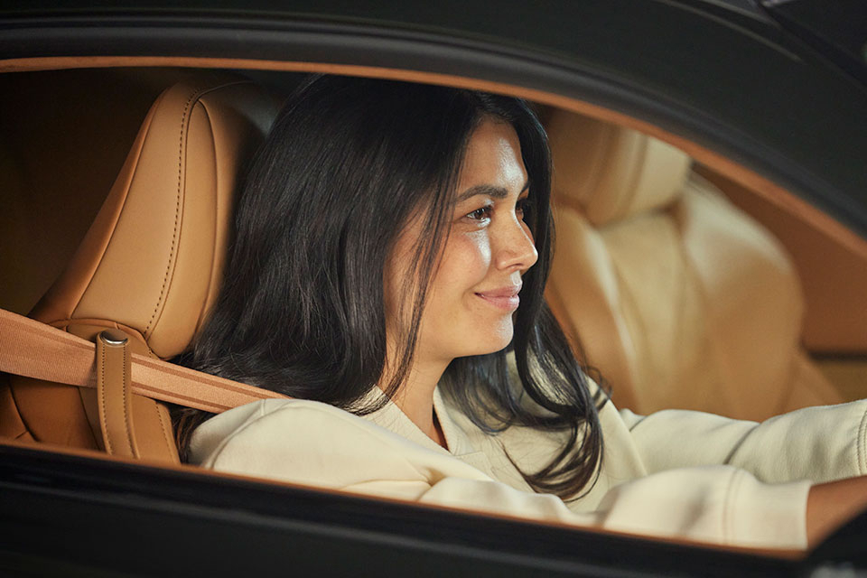 Close-up of woman smiling as she sits in the front seat of her Lexus LC, holding the steering wheel. 