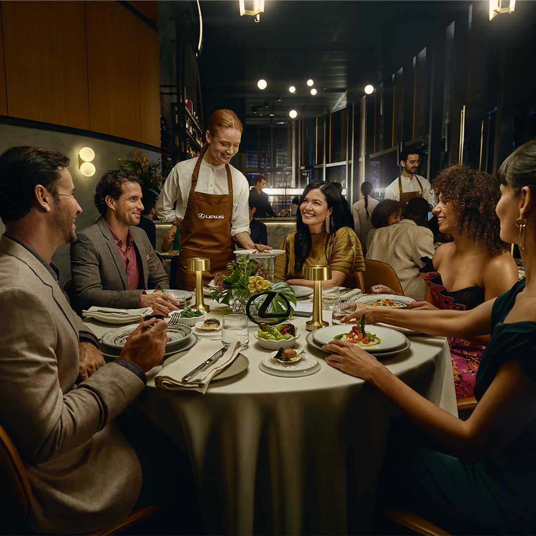 A group of friends are seated at a restaurant table and are smiling at the waiter filling their wine glasses 