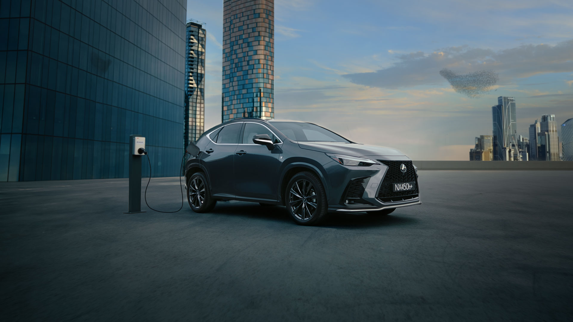 Black Lexus NX 450h+ plug-in hybrid charges with sky scrapers in the background