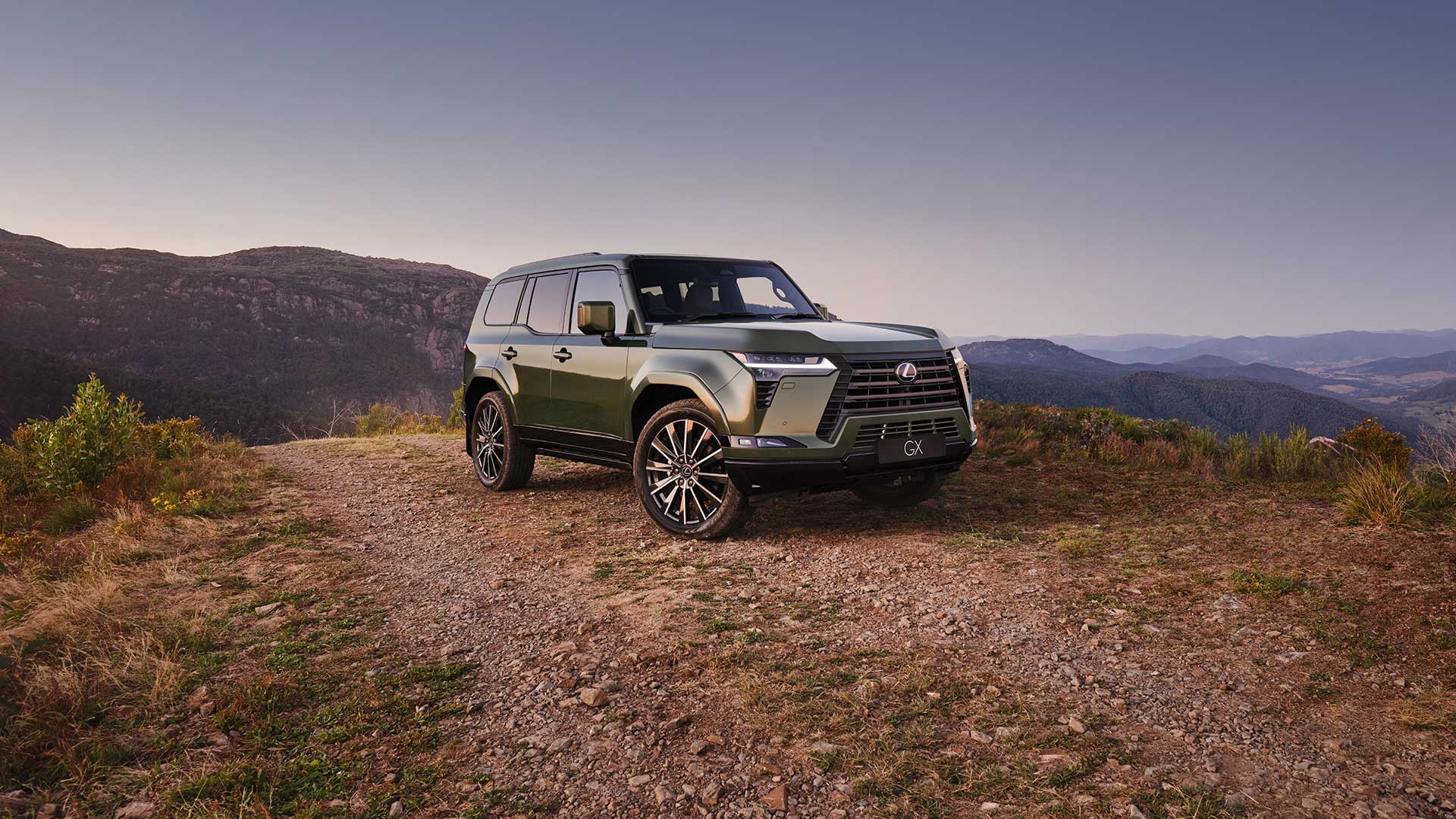 Pre-production GX Sports Luxury model shown parked on a clifftop. Blue, tree topped mountains are in the background.